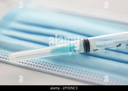 Nahaufnahme, ausgewählte Fokusansicht der Spritze auf blauer medizinischer Maske zeigt Gesundheit und Impfungen. Stockfoto