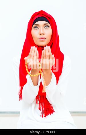 Asiatische muslimische Frau, die mit Perlen-Kette in traditionellem Kleid betet Stockfoto
