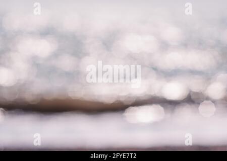 Abstrakte Natur Sommer oder Frühling Meer Meer Hintergrund. Kleine Wellen auf der goldenen, warmen Wasseroberfläche verwischen sich in Bewegung mit Bokeh-Lichtern vom Sonnenuntergang. Urlaub Stockfoto