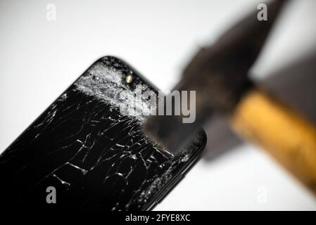 Hammer und Smartphone mit einem kaputten Bildschirm.Elektronik-Reparatur-Service. Crash-Smartphone. Innenaufnahmen geschossen. Stockfoto