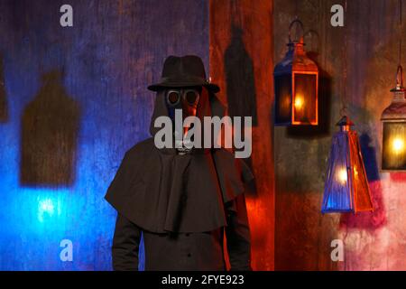 Porträt eines Pestarztes in schwarzer Ledermaske, Hut und Kapuze, isoliert an einer dunklen Wand mit Laternen. Stilisierung eines historischen Kostüms, ein gruseliges Bild, das Konzept einer Epidemie. Stockfoto