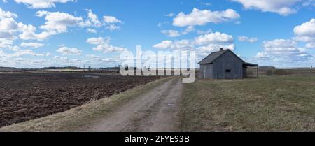 Ein altes verlassene kleines Holzhaus in den Feldern Himmel Wolken, neben einem Pfad Scheune oder gruseliges Konzept.Panoramablick. Stockfoto