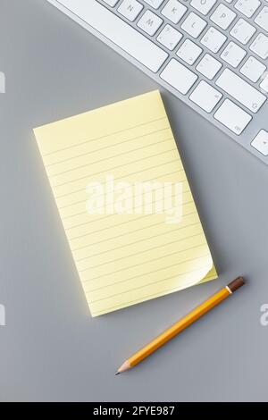 Leerer Notizblock aus Haftpapier mit Bleistift und Computertastatur auf einem grauen Tisch. Draufsicht. Stockfoto