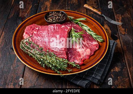 Zwei Lappen oder Flanken rohes Rindfleisch Steaks auf einem rustikalen Teller mit Kräutern. Dunkler Holzhintergrund. Draufsicht Stockfoto