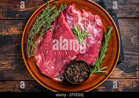 Zwei Lappen oder Flanken rohes Rindfleisch Steaks auf einem rustikalen Teller mit Kräutern. Dunkler Holzhintergrund. Draufsicht Stockfoto