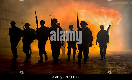 Silhouetten von Soldaten während der Militärmission in der Abenddämmerung Silhouetten von Soldaten der Armee im Nebel gegen einen Sonnenuntergang, Marines Team in Aktion Stockfoto