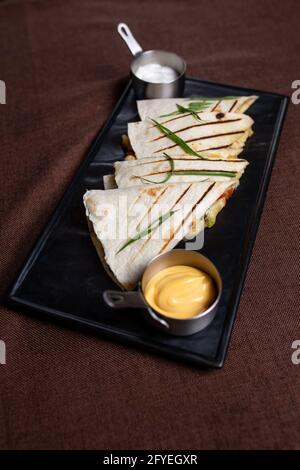 Tortillas mit Fleischfüllung und Sauce auf einem schwarzen Teller. Stockfoto