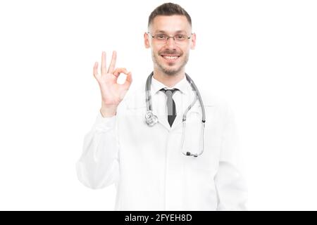 Horizontales mittleres Porträt eines erfolgreichen, gut aussehenden, jungen kaukasischen Arztes mit weißem Mantel, gestikulend vor der Kamera, weißer Hintergrund Stockfoto