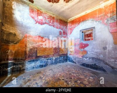 Zimmer im vierten Stil mit gelb/roten Paneelen, die durch architektonische Motive getrennt sind, alle über einem unteren schwarzen Fries - Haus des Hirschs (Casa dei Cervi) - Herculaneum Ruinen, Italien Stockfoto