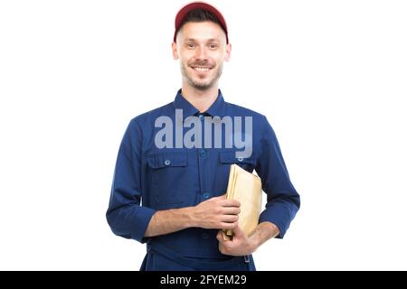 Horizontales mittleres Porträt eines hübschen jungen erwachsenen kaukasischen Lieferers, der blaue Uniform mit Umschlägen und weißem Hintergrund trägt Stockfoto