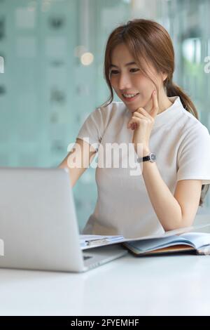 Eine kurze Aufnahme von einer freundlichen Studentin, die eine Aufgabe mit der Universität macht Laptop und Schreibwaren in moderner Bibliothek Stockfoto