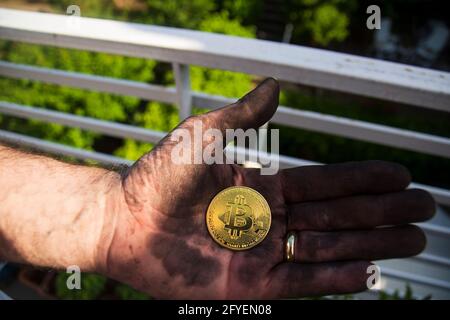 Ein Bergmann zeigt stolz sein neu abgebautes und mit Bitcoin behaltenes Stück unter schwarzen Kohlen. Selektive Fokusmünze. Stockfoto