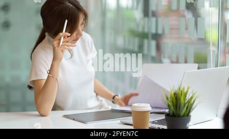 Eine kurze Aufnahme von einer nachdenklichen Studentin, die mit einer Universität eine Aufgabe macht Laptop und Schreibwaren in der Bibliothek Stockfoto