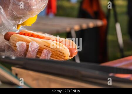 Frischer Hot Dog mit gebratener Wurst, serviert in einem Café im Freien. Kochen amerikanischer Grillgerichte. Der Koch füllt einen Hot Dog mit Senf. Grillfest Stockfoto