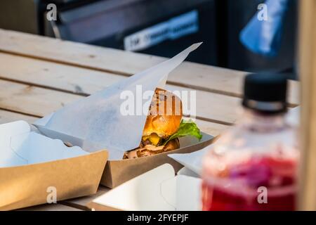 Saftiger Cheeseburger mit Rinderpasteten in einer Take-away-Verpackung auf der Theke eines Straßenhandels. Grillfest im Stadtpark. Street Fast Food. Stockfoto