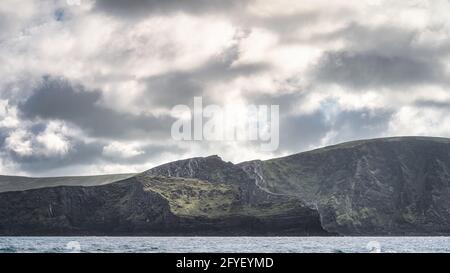 Wunderschöne, hohe Kerry Cliffs im Morgenlicht mit dramatischem Himmel, vom Boot aus gesehen auf dem Atlantik, Portmagee, der Halbinsel Iveragh, Ring of Kerry, Irland Stockfoto