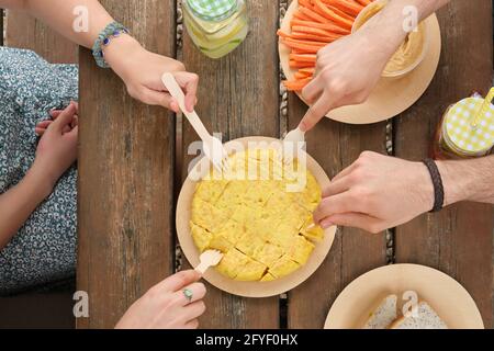 Eine Gruppe von unwiedererkennbaren, glücklichen Freunden, die an einem sonnigen Sommertag ein Stück spanisches Omelett mit einer Gabel in einem Park zum Picknick nehmen. Draufsicht. Stockfoto