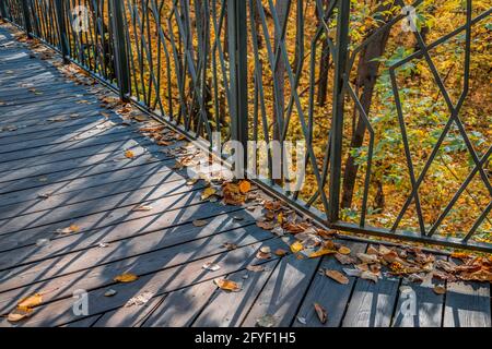 Draufsicht auf einen Teil der alten Holzbrücke in Der Stadtpark ist mit gefallenen gelben Herbstblättern bedeckt Stockfoto