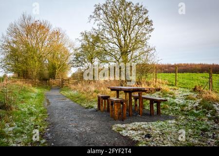 Holztisch und Stühle im Winter auf einem Sitzbereich auf einem Landweg, mit Frost auf dem Boden, Dumfries und Galloway, Schottland Stockfoto