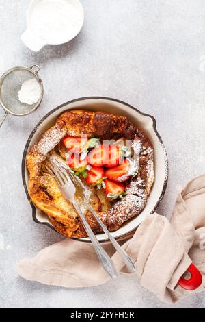 Holländischer Baby-Pfannkuchen mit frischer Erdbeerbeere und bestreut mit Puderzucker-Pulver in roter Pfanne auf weißem Küchenhintergrund. Draufsicht Stockfoto