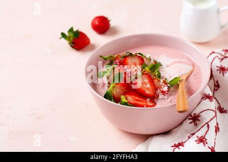 Frühstück mit Müsli, Kokosnuss und Erdbeer-Smoothie in einer Schüssel auf einem rosa hellen Hintergrund. Frühjahrs-Diät-Menü.Draufsicht Stockfoto