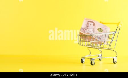 Einkaufswagen und eine tausend Thai Baht Note auf gelbem Hintergrund, Nahaufnahme. Black Friday Shopping- und Rabattkonzept Stockfoto