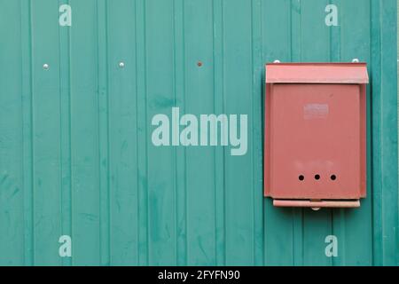 Eine alte orangefarbene Metallmailbox auf dem eisernen grünen Zaun eines Landhauses. Stockfoto