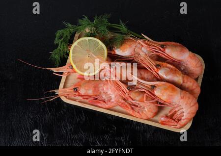 Gekochte Garnelen in einer Schale mit Dill und Zitrone in einer Holzschale auf dunklem Holzgrund. Selektiver Fokus. Stockfoto