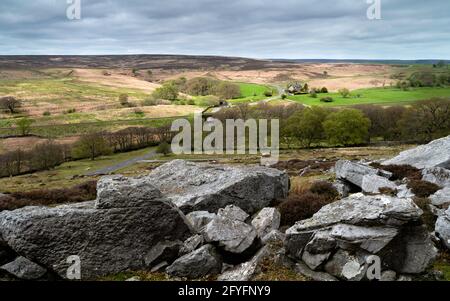 Die North York Moors mit Steinblöcken, Heidekraut, Bäumen, Feldern und Hauptstraße, die durch die ländliche Landschaft in der Nähe von Goathland, Yorkshire, Großbritannien, führt. Stockfoto