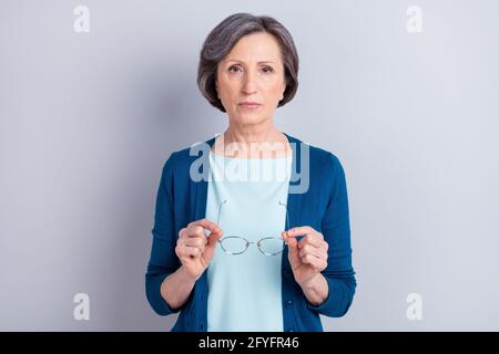 Fotoporträt einer ernsthaften älteren Frau, die eine blaue Brille trägt strickjacke isoliert auf grauem Hintergrund Copyspace Stockfoto