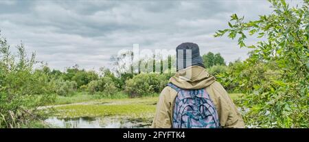 Aktiver Mann im Mückenanzug mit Rucksack beim Wandern in der Nähe des Waldsees. Alleinreisende, Lifestyle, inländisches Tourismuskonzept Stockfoto