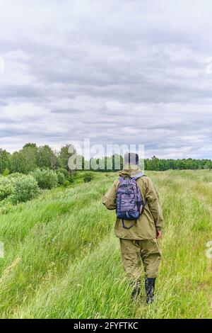 Aktiver Mann im Mückenanzug mit Rucksack beim Wandern auf einer Wiese. Alleinreisende, Lifestyle, inländisches Tourismuskonzept Stockfoto