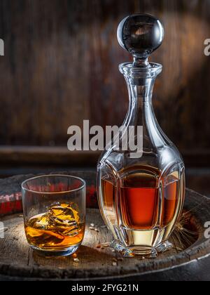 Karaffe Whisky und Glas Whisky auf altem Holzfass auf dunklem Hintergrund. Stockfoto