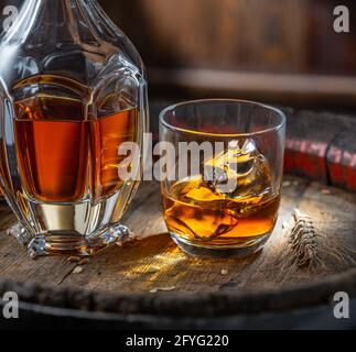 Karaffe Whisky und Glas Whisky auf altem Holzfass auf dunklem Hintergrund. Stockfoto