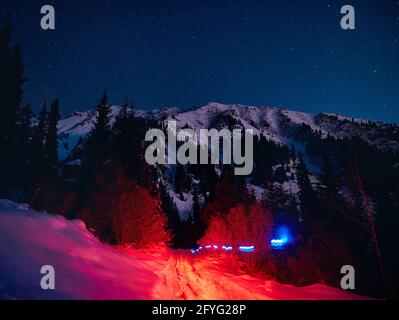 Abstrakter Strahl aus rot und blau leuchtenden Lichtern auf dem Straße im Winter verschneiten Wald in den Bergen unter Nacht Himmel mit Sternen Stockfoto