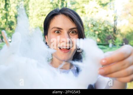 Das Brünette Mädchen in Bewunderung reißt ein Stück Zuckerwatte ab. Freuen Sie sich auf süße Speisen, heiße Rabatte in Geschäften und ein Sonderangebot Stockfoto