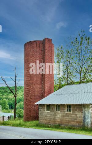 Altes Ziegelsilo vor einem wunderschönen blauen Himmel neben einem Blockgebäude. Stockfoto