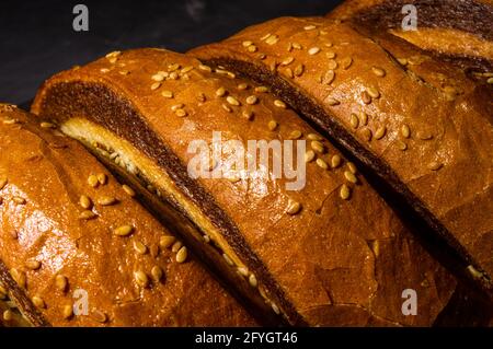 Ungewöhnlicher zweifarbiger frischer Laib Brot auf schwarzem Hintergrund, Foto in einer niedrigen Taste bei hartem Licht, Nahaufnahme Stockfoto