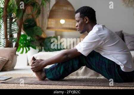 Afrikanischer junger Mann sitzt in Paschimottanasana oder intensive dorsale Stretch-Pose, sitzend nach vorne beugen Haltung Stockfoto