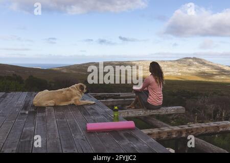 Nachdenkliche kaukasische Frau, die auf der Terrasse sitzt und den Hund bewundert Die Aussicht in ländlicher Berglandschaft Stockfoto