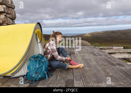 Fröhliche kaukasische Frau, die im Zelt auf der Bergterrasse sitzt und Socken anlegt Stockfoto