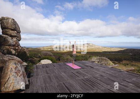 Kaukasische Frau, die Yoga praktiziert, steht auf einem Bein und dehnt sich ein Ländliche Berglandschaft Stockfoto