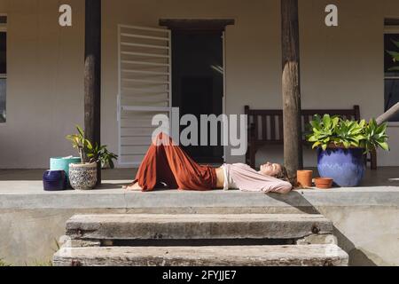 Glückliche kaukasische Frau, die sich auf der sonnigen Cottage-Terrasse entspannt Stockfoto