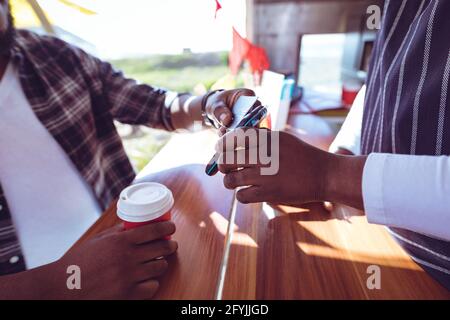 Mittelteil des afroamerikanischen Mannes in Food Truck mit Smartphone Zahlungsterminal Stockfoto