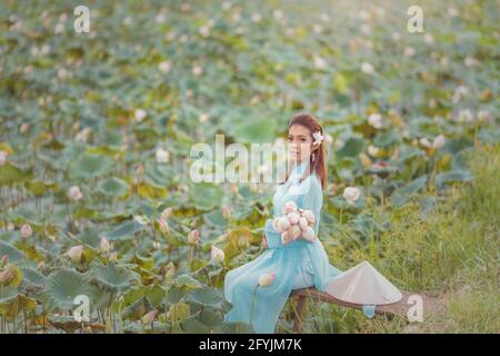 Porträt einer schönen Frau in einem traditionellen konischen Hut mit einem Strauß Seerosenblumen, Thailand Stockfoto