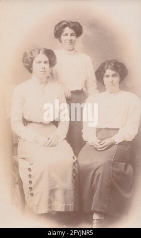 Alte Fotopostkarte aus dem frühen 20. Jahrhundert, die eine drei Damen zeigt. Möglicherweise eine Mutter und ihre beiden Töchter. Alle haben ähnliche Frisuren. Stockfoto