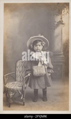 Vintage Fotopostkarte aus dem frühen 20. Jahrhundert, die ein schönes junges Mädchen in ihrem Mantel und ihrer Haube zeigt. Stockfoto