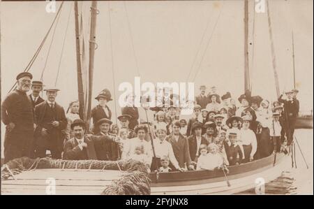 Eine alte Fotopostkarte aus dem frühen 20. Jahrhundert zeigt eine Gruppe glücklicher Passagiere auf einem Boot für einen Ausflug. Stockfoto