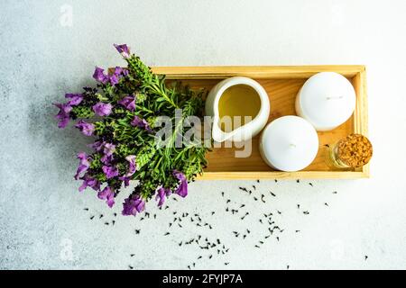 Blick von oben auf frische Lavendelblüten auf einem Tablett neben einem Krug mit Öl und zwei Blockkerzen Stockfoto