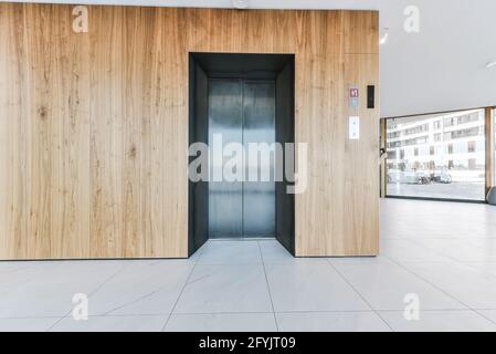 Eingangshalle des luxuriösen Apartmentgebäudes mit Holzwandpaneelen Und Aufzug vor Panoramafenstern Stockfoto